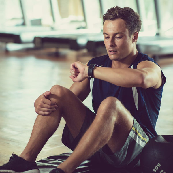 Man sitting on a gym floor checking his watch