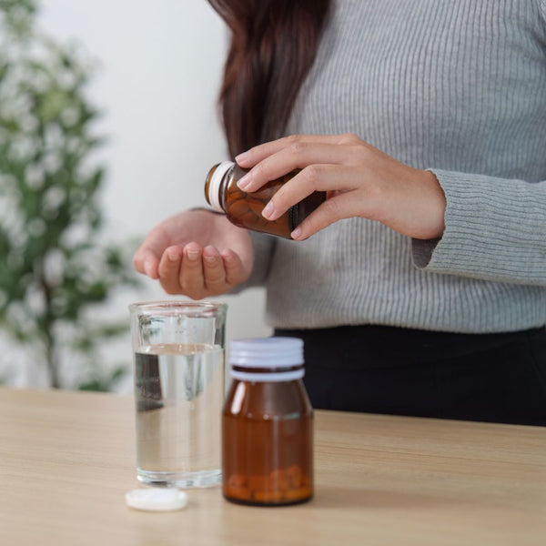Person holding a bottle of syrup over a glass of water on a table.