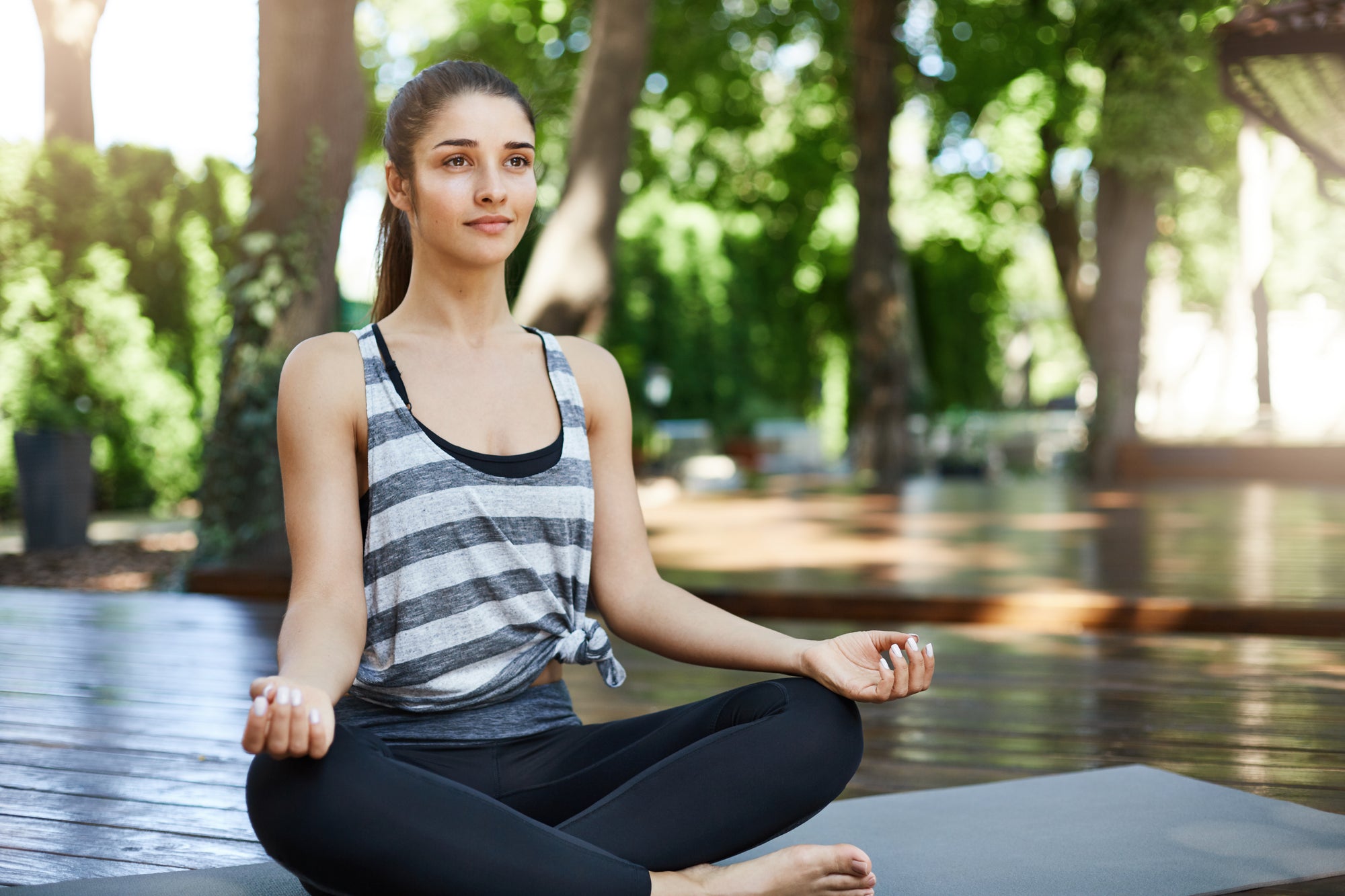 Woman meditating outdoors on a wooden deck with greenery in the background